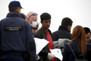 Un funcionario de la UE sostiene la documentación de un migrante (centro) en un barco que les traslada de regreso a Turquía desde Lesbos, este viernes.-REUTERS / GIORGOS MOUTAFIS