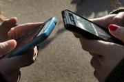 Una foto de archivo con dos personas escribiendo en sus teléfonos móviles.-FERRAN NADEU