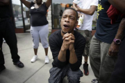 Un hombre reza mientras la policía dispersa a los manifestantes en Ferguson tras el asesinato de Michael Brown.-Foto:  AP / Jeff Roberson