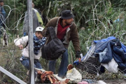 Varios migrantes cruzan la alambrada por un agujero cerca de Roszke (Hungría), en la frontera con Serbia, este jueves.-AFP / ATTILA KISBENEDEK