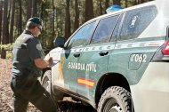 Agente de la Benemérita junto a un vehículo policial en un monte.