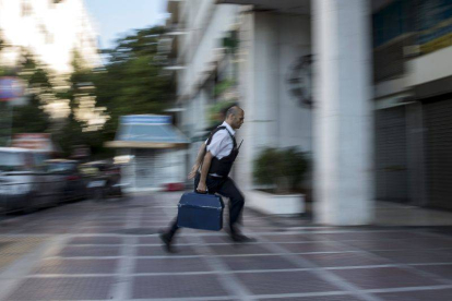 Un hombre entra dinero con una maleta en una sucursal bancaria de Atenas.-Foto: REUTERS / MARKO DJURICA