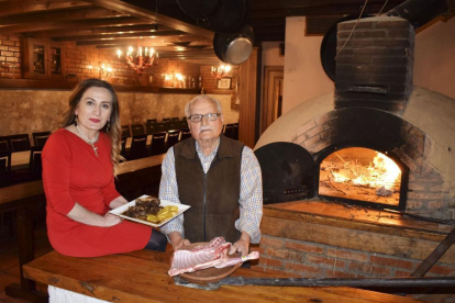 Olga y su padre, José Camarero, con un plato de carne estofada y el lechazo con IGP, junto al horno de asar del restaurante.-ARGICOMUNICACIÓN