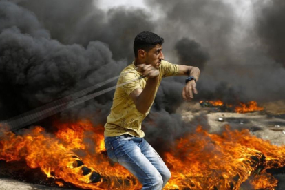 Un palestino se dispone a lanzar piedras entre los neumáticos incendiados contra las tropas israelís, en las protestas junto a la frontera de la Franja de Gaza, el 20 de abril.-/ AFP / MOHAMMED ABED