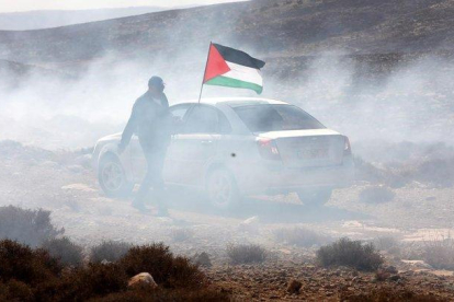 Un hombre ondea la bandera palestina entre gas lacrimogeno en el pueblo cisjordano de Shiyoukh.-ABED AL HASHLAMOUN (EFE)