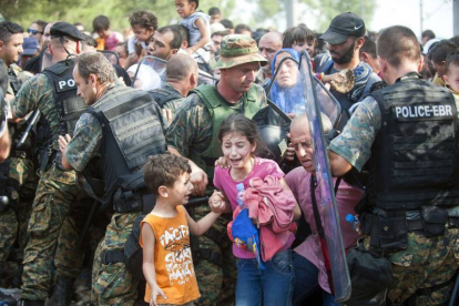 Varios refugiados ayudan ayer a uno de sus compañeros que muestra su desesperación con un niño en brazos frente a la policía de Macedonia.-Foto: AP/ D. V.