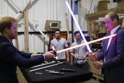 Los príncipes Enrique y Guillermo juegan con las espadas de luz de Star Wars en su visita a los estudios de Londres donde se está rodando la octava entrega de la saga.-EL PERIÓDICO (AP / ADRIAN DENNIS)