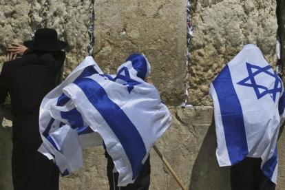 Jóvenes israelís se cubren con la bandera de Israel junto a un untraortodoxo frente al Muro de las Lamentaciones. /-AP / DAN BALILTY
