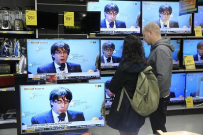 Una pareja sigue la rueda de prensa de Puigdemont en una tienda del Poblenou.-/ FERRAN NADEU