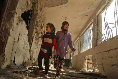 Dos niñas sirias recorren su escuela, destrozada el día anterior por los ataques áereos de la aviación gubernamental, en la sitiada ciudad de Saqba (Guta Oriental), el 9 de noviembre.-/ AFP / AMER ALMOHIBANY