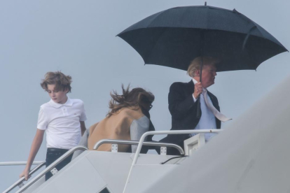 El presidente de EEUU, Donald Trump, sostiene un amplio paraguas para protegerse de la lluvia, mientras espera a su mujer Melania y a su hijo Barron, durante el embarque del Air Force One en Flordia.-/ AFP / NICHOLAS KAMM (AFP)