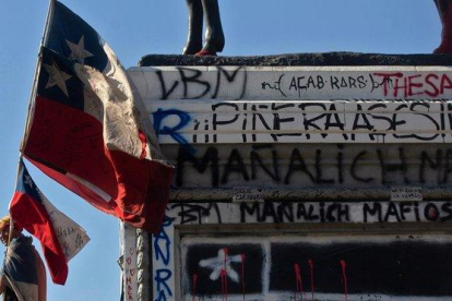 Un manifestante con una bandera de Chile pasa junto a la base de una estatua ecuestre repleta de pintadas.-CLAUDIO REYES (AFP)