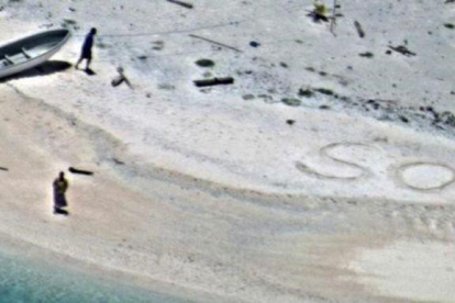 SOS escrito en la arena de playa por  Linus y Sabina Jack.-US NAVY