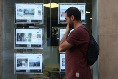 Un joven mirando ofertas de pisos de alquiler en los expositores de una inmobiliaria de Barcelona.-ELISENDA PONS