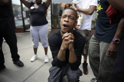Un hombre reza mientras la policía dispersa a los manifestantes en Ferguson tras el asesinato de Michael Brown.-Foto:  AP / Jeff Roberson