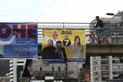 Ciudadanos caminan frente a varios carteles electorales en Quito.-EFE / JOSÉ JACOME