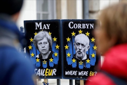 Unos peatones pasan junto a carteles con la primera ministra británica, Theresa May, y el líder del Partido Laborista, Jeremy Corbyn, cerca del Parlamento, en Londres.-TOLGA AKMEN (AFP)