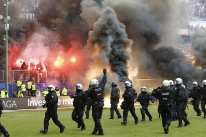 Antidisturbios saltan al césped del estadio del Hamburgo mientras en la grada se queman camisetas y banderas.-AP / MICHAEL SOHN