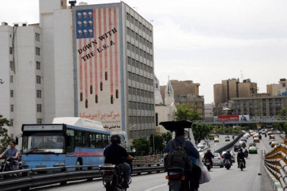 Conductores iranís circulan junto a un edificio en el que aparece una pintada contra Estados Unidos en Teherán.-EFE / ADEDIN TAHERKENAREH