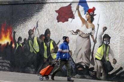 Un hombre pasa junto a un mural que reproduce una versión de La libertad guiando al pueblo, de  Eugene Delacroix, con la presencia de chalecos amarillos, idea del artista Pascal Boyart.-GETTY IMAGES