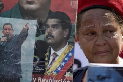 Una partidaria del chavismo llora mientras sostiene imágenes de Chávez y Maduro, durante una marcha por el quinto aniversario de la muerte de Chávez, en Caracas, el 15 de marzo.-AP / FERNANDO LLANO