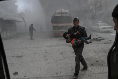 Un voluntario de los Cascos Blancos sirios lleva a un niño herido en brazos hasta una ambulancia, tras un bombardeo en Duma (Guta Oriental), el 22 de febrero.-/ EFE / MOHAMMED BADRA
