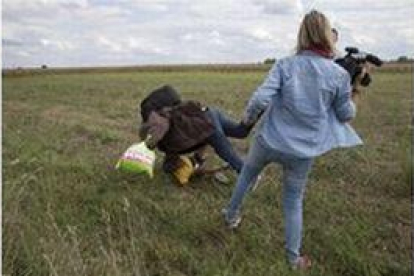 Petra Laszlo le hace la zancadilla a un padre que lleva en brazos a su hijo y una bolsa con sus pertenencias, en Roszke (Hungría).-MARKO DJURICA / REUTERS