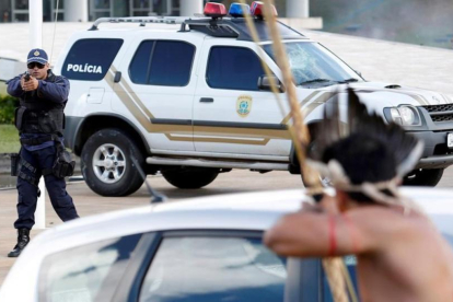 Un policía apunta con su arma a un indígena armado con un arco y flechas frente al Congreso de Brasilia.-REUTERS / GREGG NEWTON