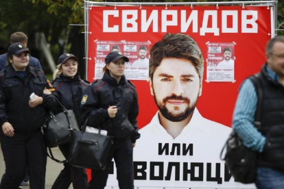 Varias personas pasan junto a un póster electoral del partido nacionalista Rodina (Patria), en Moscú, este jueves.-AP / PAVEL GOLOVKIN