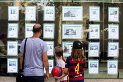 Un hombre y dos niñas observan las ofertas de viviendas en una agencia inmobiliaria del paseo de Maragall de Barcelona.-ARCHIVO / FERRAN NADEU