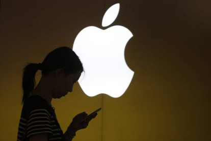 Una mujer mira su teléfono ante el logo de Apple en la tienda oficial de Shangai, China.-Foto: REUTERS / ALY SONG