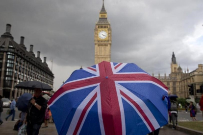 Un transeúnte se refugia de la lluvia en un paraguas con la bandera británica, cerca del Big Ben.-AFP / JUSTIN TALLIS