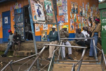 Un grupo de kenianos junto a un local con la fachada cubierta de carteles durante la campaña electoral-AP / JEROME DELAY