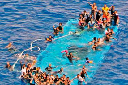 Momento del rescate de los migrantes que esperan sobre el casco de la embarcación.-
