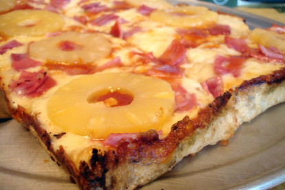 Una porción de pizza hawaiana, con rodajas de piña enteras.-