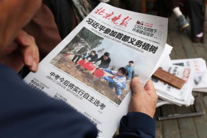 Un hombre lee un periódico donde aparece en portada el presidente Xi en una plantación de árboles, el 6 de abril, en Pekín.-AFP