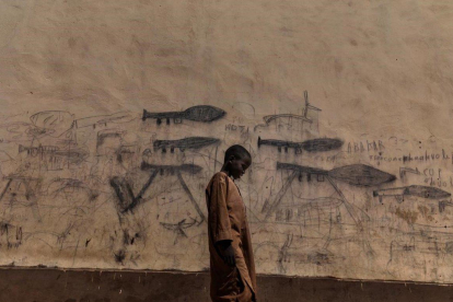 Un chico huérfano pasa junto a un mural con dibujos de lanzagranadas en Bol, Chad. / MARCO GUALAZZINI (CONTRASTO)
