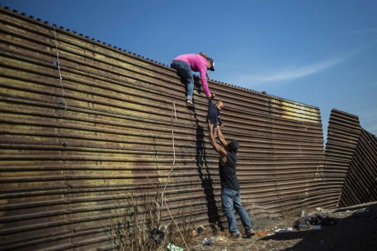 Inmigrantes suben a la valla entre México y Estados Unidos cerca del puesto fronterizo de El Chaparral, en Tijuana, México. / PEDRO PARDO (AFP)