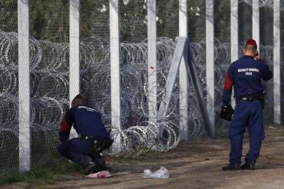 Policías húngaros reparan una agujero en la alambrada de la frontera con Serbia.-AP / MATTHIAS SCHRADER