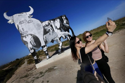 Turistas se acercan a fotografiarse y observar el toro de Osborne que ha aparecido pintado con el escenas del Guernica de Picasso en Santa Pola, Alicante.-EFE