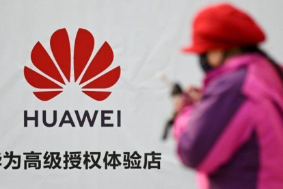 Una mujer consulta su smartphone junto a un cartel publicitario de Huawei, en una calle de Pekín.-WANG ZHAO (AFP)