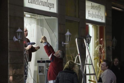 Unos hombres reparan los escaparates de una tienda rotos por los manifestantes ultraderechistas en Leipzig.-AFP / JAN WOITAS