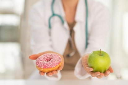 Una doctora dando a elegir entre un donut o una manzana.-123RF
