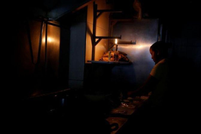 Una mujer usa la luz de una linterna para trabajar en la cocina de un restaurante tras un nuevo apagón en Caracas.-CARLOS GARCÍA RAWLINS (REUTERS)