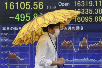 Un hombre pasa ante un sociedad de bolsa en Tokio en cuyo paneles informativos se muestra la caída del mercado.-Koji Sasahara