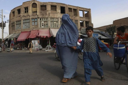 Una mujer afgana vestida con un burka agarra de la mano a su hijo al cruzar una calle en Herat, Afganistán, este jueves.-EFE / JALIL REZAYEE