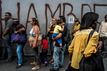 Venezolanos hacen cola frente a una pintada con la palabra hambre, en Caracas.-JUAN BARRETO (AFP)