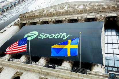 El logo de Spotify cuelga de la fachada de la Bolsa de Nueva York entre la bandera de Estados Unidos y la Sueca, país en el que la plataforma número uno de música en internet fue fundada y tiene su sede.-/ HANDOUT (REUTERS)