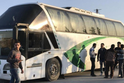 Varias personas permanecen junto a un autobús a la espera de la llegada del resto de evacuados civiles y combatientes.-EFE / MOHAMED BADRA