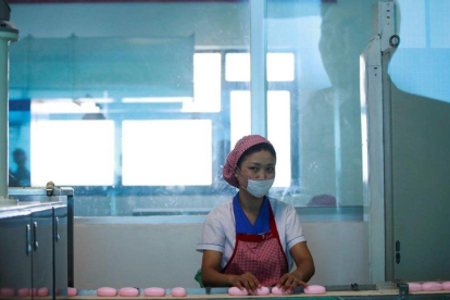 La silueta de un hombre aparece reflejada en el cristal mientras una empleada norcoreana trabaja en la cadena de produccion de jabones de la Fabrica de Cosmética de Pionyang, el 8 de septiembre del 2018.-EFE